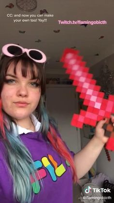 a girl with blue hair and pink glasses holding up a red pixelo - style object