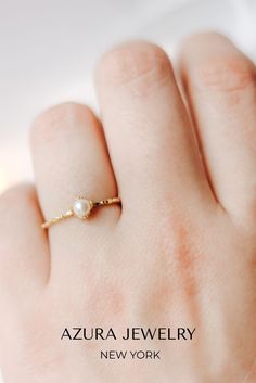 a woman's hand wearing a gold ring with a white pearl on the middle