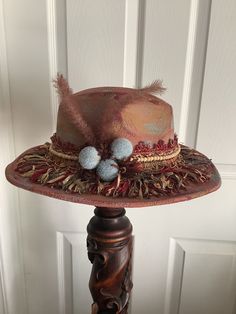 This is a custom weathered hat with incredible detail.  Tan felted  hat weathered in red, gold and blue.  Incredible fringe trim is a show stopper.  Also has a wood beaded trim, ferns, flowers, blue flower pins and a vintage pin and button. Adjustable band in side. Vintage Fedora Mini Hat For Festivals, Handmade Vintage Felt Hat For Kentucky Derby, Bohemian Red Hats For Kentucky Derby, Bohemian Red Hat For Kentucky Derby, Red Bohemian Hat For Kentucky Derby, Bohemian Fedora Hat With Fringe, Bohemian Hat With Fringe And Curved Brim, Bohemian Fringe Fedora Hat, Vintage Hats For Kentucky Derby Festival