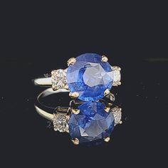 an oval shaped blue sapphire and diamond ring on a black surface with gold trimmings