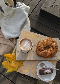 a bagel and coffee on a wooden tray with autumn leaves next to the table