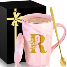 a pink marbled coffee mug next to a black box with gold lettering and a spoon