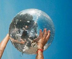 two people reaching up to grab a disco ball in the air with their hands, against a blue sky