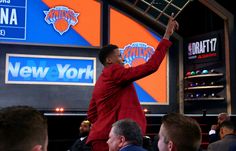 a man standing on top of a chair in front of a large screen with the new york mets logo