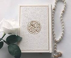 a white rose sitting next to a card with an arabic writing on it and a pearl necklace