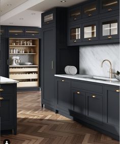 a kitchen with black cabinets and marble counter tops, gold pulls on the cupboards