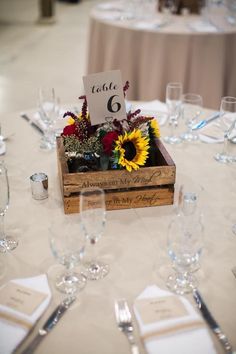 a wooden box filled with flowers on top of a table covered in white linens