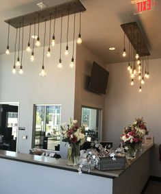 a counter with flowers in vases and lights hanging from it's ceiling above