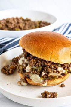 a sloppy joe sandwich on a plate with a bowl of ground beef in the background