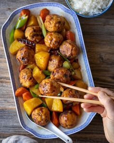 someone is holding chopsticks over some meatballs and veggies on a plate