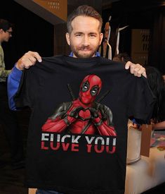 a man holding up a deadpool t - shirt with the words euck you on it