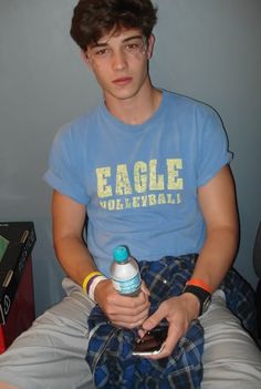 a young man sitting down holding a water bottle and cell phone