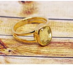 two gold rings sitting on top of a wooden table with a yellow stone in the middle