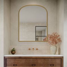 a bathroom with a large mirror above the sink and wooden drawers below it, along with a vase filled with flowers