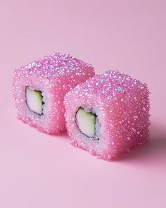 two sushi rolls covered in pink glitters on a pink background with one cut in half