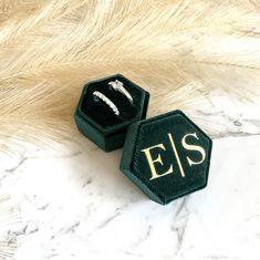 two black velvet jewelry boxes sitting on top of a white marble table with gold lettering