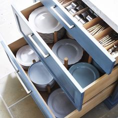 an open cabinet filled with dishes and silverware on top of a tiled countertop