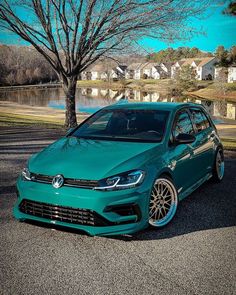 a green volkswagen car parked in front of a lake with houses and trees behind it