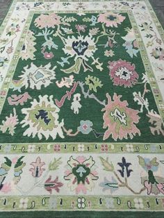 a green rug with pink and blue flowers on the bottom is sitting on a wooden floor