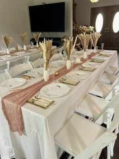 a long table set with white plates and gold place settings for an elegant dinner party