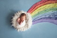 a baby wrapped in a blanket is laying on top of a rainbow - colored backdrop