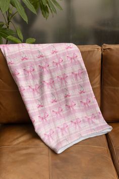 a pink and white blanket sitting on top of a brown couch next to a potted plant