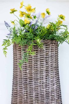 a wicker basket filled with flowers on top of a wooden table next to a white wall