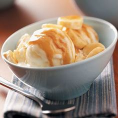 a bowl filled with bananas and ice cream on top of a wooden table next to a spoon