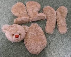 a teddy bear laying on the floor next to four pairs of slippers