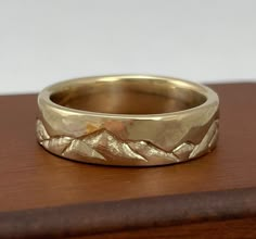 a gold wedding band with mountains in the background on a wooden surface, close up