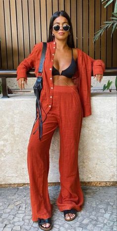 a woman standing next to a wall wearing an orange jumpsuit and black bra top