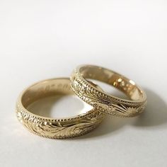 two gold wedding rings sitting side by side on a white surface with one ring in the middle