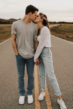 a man and woman kissing on the side of an empty road while standing next to each other