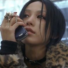 a woman talking on a cell phone while wearing a leopard print coat and holding an object in her hand