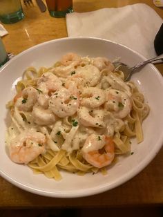 pasta with shrimp and cream sauce in a white bowl on a wooden table next to silverware