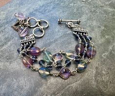 Three layers of soft hues of pink, purple, lavender and London blue make this a soothing and calming bracelet. The stones make it a powerful protector. The two outer layers consists of central, faceted pink amethyst links in sterling silver accented by faceted rainbow fluorite ovals. They are wire wrapped to 3 strand pewter links with London blue Swarovski crystals. The middle layer is the same London wire wrapped crystals. The bracelet closes with an adjustable toggle clasp in sterling silver. At the end of clasp is a sterling heart charm and two faceted pink amethyst briolette. It extends from 6 to 7 1/4 inches. The last picture shows the bracelet stacked with a silver cuff. This listing is for the multi strand beaded bracelet only. Amethyst: Calming and protective: Helps facilitate deci Handmade Purple Multi-strand Bracelets, Handmade Purple Multi-strand Bracelet, Wire Wrapped Crystals, Wrapped Crystals, Fluorite Bracelet, Wire Wrapping Crystals, Multi Strand Bracelet, Purple Lavender, Amethyst Bracelet