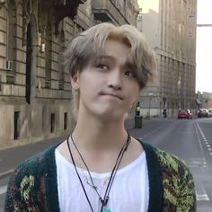 a young man standing on the side of a street next to tall buildings and looking at the camera