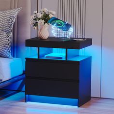 a night stand with two drawers and a vase on it, next to a bed