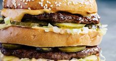 a cheeseburger with pickles and onions on a sesame seed bun is stacked high