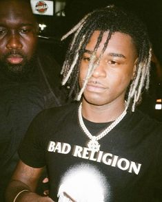 a man with dreadlocks standing next to another man wearing a black t - shirt