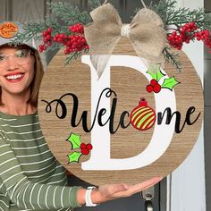 a woman holding up a wooden sign with the word'd'and christmas decorations on it