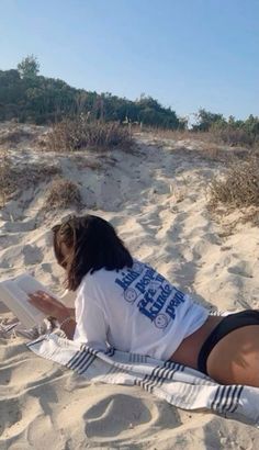 a woman laying in the sand reading a book