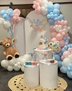 a teddy bear sitting on top of a cake table next to balloons and desserts