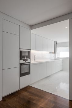 an empty kitchen with white cabinets and wood floors