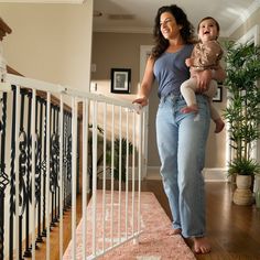 a woman holding a baby in her arms while standing next to a stair rail with railings on both sides