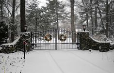 an iron gate with wreaths on it in the middle of a snow covered yard