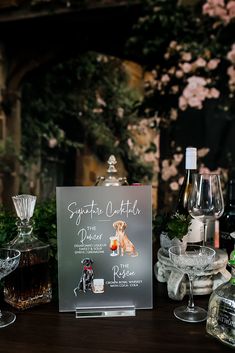 there is a sign on the table with wine glasses and bottles in front of it