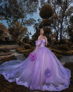 a woman in a purple dress is posing for the camera with trees and bushes behind her