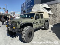 a jeep with a tent on the roof is parked in front of a building and people are looking at it