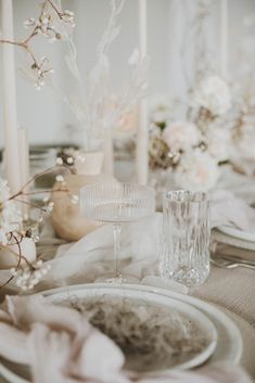 the table is set with white flowers and candles in vases, plates and silverware